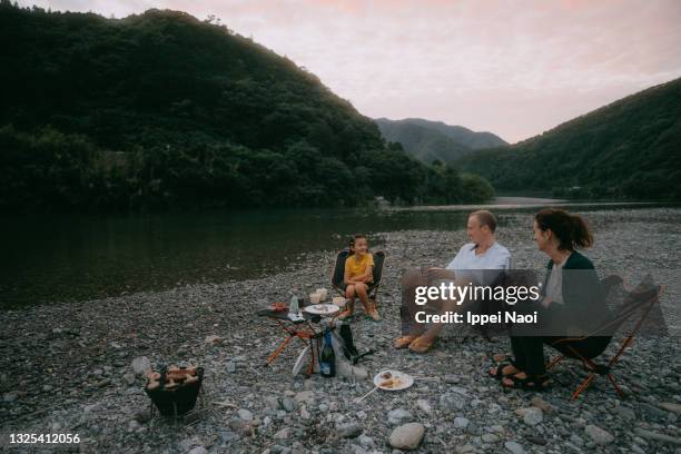 family enjoying bbq dinner at riverside campsite - camping chair stock pictures, royalty-free photos & images