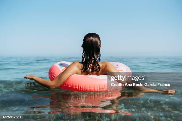 young woman in a sprinkled doughnut float at the beach - malaga beach stock pictures, royalty-free photos & images