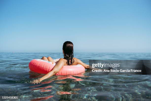 young woman in a sprinkled doughnut float at the beach - relax holiday stock pictures, royalty-free photos & images
