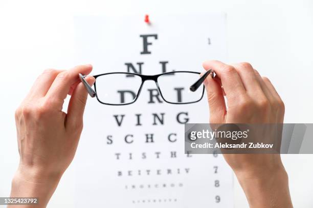 modern fashion glasses in the hands of a woman or girl, next to the diagram of the snellen vision test. ophthalmology, visual acuity testing, treatment and prevention of eye diseases. the concept of poor vision, blindness, treatment of an ophthalmologist. - sehtest stock-fotos und bilder