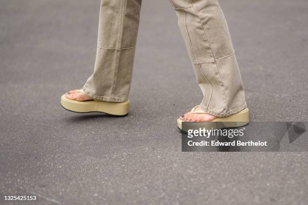 Alice Barbier wears pale khaki patched / ripped flared denim jeans pants, pale yellow / beige matte leather flip-flops / sandals shoes with platform...