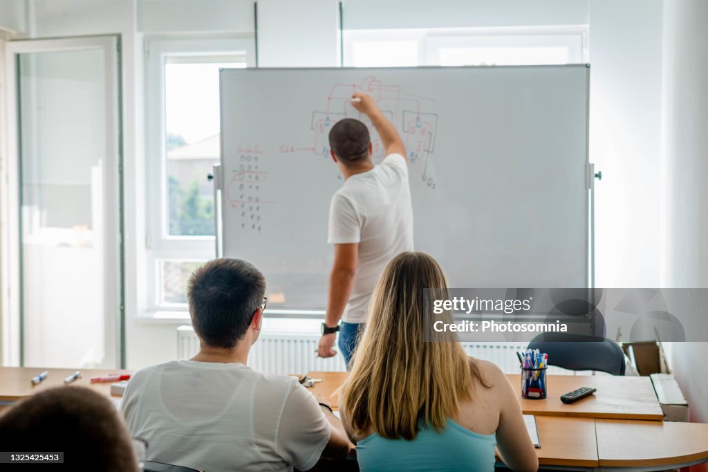 Small group of students sitting in the lecture hall at university and listening to their young teacher