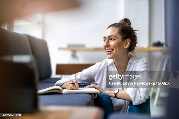 smiling businesswoman writing in book while sitting at desk in office,warsaw,poland - daily life in warsaw photos et images de collection