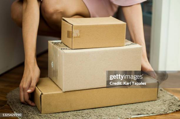 a young southeast asian woman is picking up carton packages on the front door - online shopping stock pictures, royalty-free photos & images