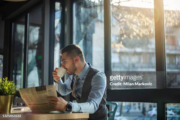 ein junger geschäftsmann, der eine pause von der arbeit eingeht, verbringt zeit in einem café. - newspaper luxury stock-fotos und bilder