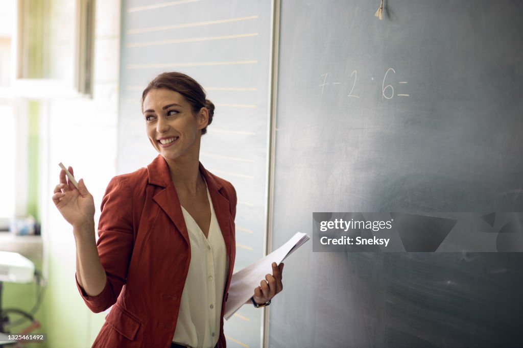Teacher writing on blackboard in classroom.