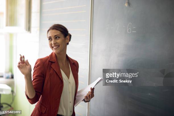 teacher writing on blackboard in classroom. - teacher stock pictures, royalty-free photos & images