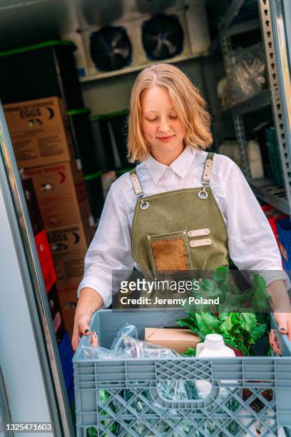 ritratto di una giovane donna caucasica felice in piedi alla porta di un frigorifero walk-in che tiene un cesto di prodotti deliziosi, sani e biologici in un fornitore locale di piccole imprese farm-to-table in colorado - homegrown produce foto e immagini stock