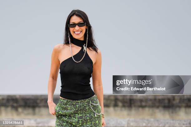 Bella Hadid wears sunglasses with a bejeweled / diamonds chain, a black off-shoulder cropped mesh top with turtleneck, green leather snake print...