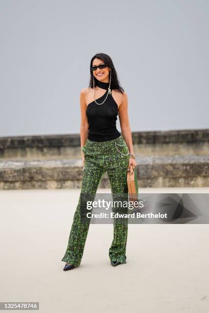 Bella Hadid wears sunglasses with a bejeweled / diamonds chain, a black off-shoulder cropped top with turtleneck, green leather snake print pattern...