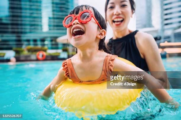happy little asian girl with sunglasses smiling joyfully and enjoying family bonding time with mother, having fun in the swimming pool on summer vacations - family pool stock-fotos und bilder