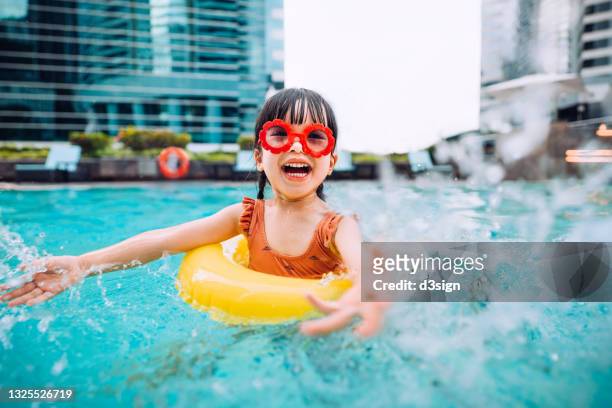 playful little asian girl with sunglasses smiling joyfully, splashing and playing with water happily in the swimming pool on summer vacations - children in summer photos et images de collection