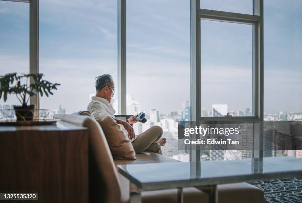 asian chinese retired senior man relaxing at living room looking at his camera and digital tablet - chinese people posing for camera stockfoto's en -beelden