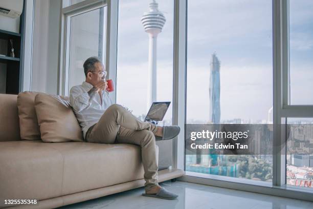 asiatico cinese in pensione senior man rilassante in soggiorno bevendo caffè guardando fuori dalla finestra con kl tower città di kuala lumpur - apartment living asian foto e immagini stock