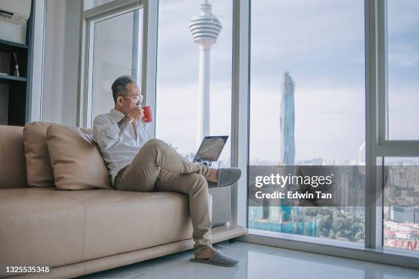 asian chinese retired senior man relaxing at living room drinking coffee looking outside the window with kl tower city of kuala lumpur - capital building imagens e fotografias de stock