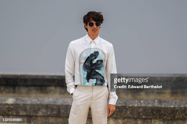 Germain Louvet wears black sunglasses, a white shirt with a black and blue painted window, beige suit pants, a silver ring, outside Dior, during...