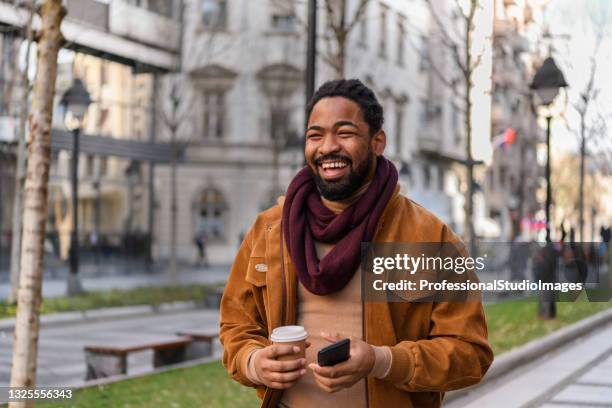 portrait of a handsome african man with coffee walking in the city streets. - a fall from grace 個照片及圖片檔