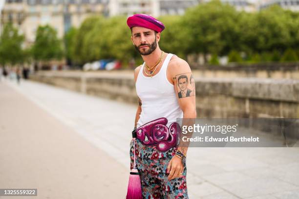 Pelayo Diaz wears gold earrings, a fuchsia / purple /and white print patter wool felt beret / hat, a gold chain necklace, a white pearls necklace,...