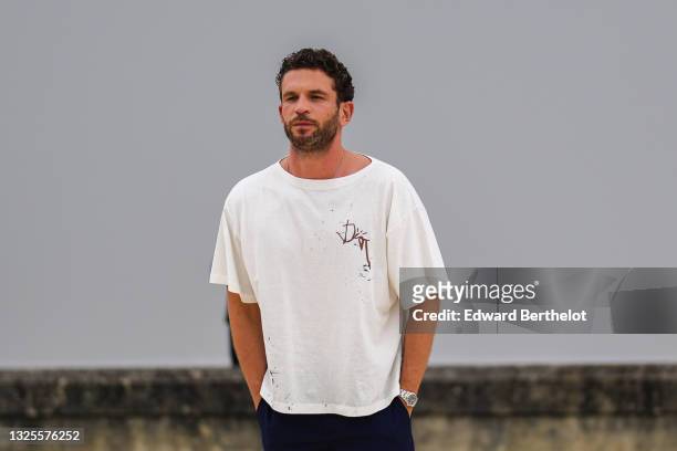 Arnaud Valois wears a white oversized t-shirt with a brown Dior embroidered, navy blue suit pants, a silver watch, outside Dior, during Paris Fashion...