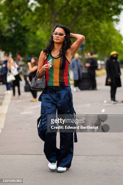 Guest wears white Chanel sunglasses, gold chain necklaces, a black bra underwear, a green yellow red and black striped mesh tank-top, a black shiny...