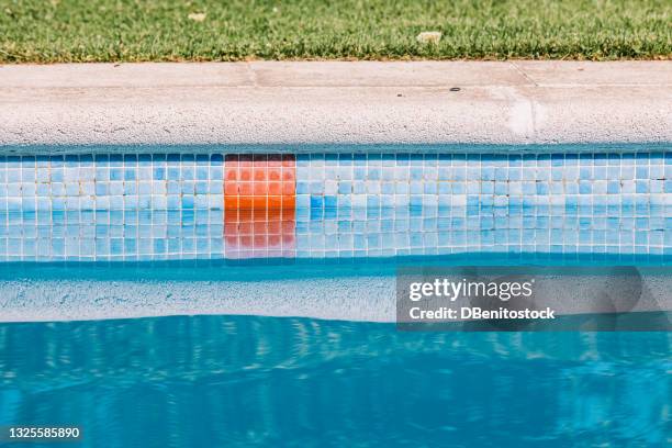 detail of the edge of the pool with blue tiles and a red stripe indicating the deep area, on a sunny summer day - poolside stock-fotos und bilder
