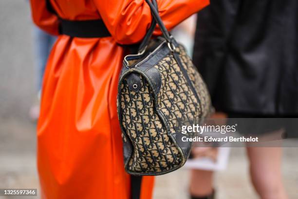 Guest wears a neon orange leather long dress, a black belt, a blue and beige Dior Oblique Jacquard handbag from Dior, outside Dior, during Paris...