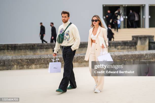 Guest wears a beige wool turtleneck pullover with purple orange and blue embroidered pattern, a dark green Dior Oblique Jacquard leather fanny pack...