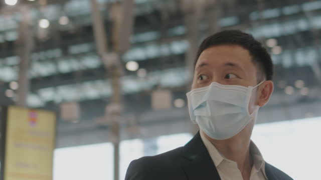 Chinese businessman with protective face mask talk to his friend and walk in the airport - stock video