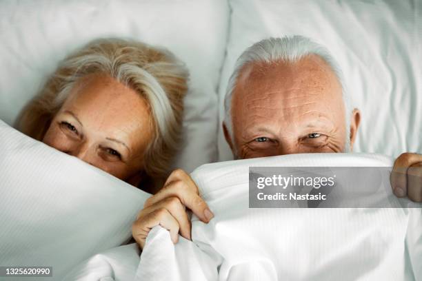 happy senior couple relaxing in bed hiding under sheets - par säng bildbanksfoton och bilder