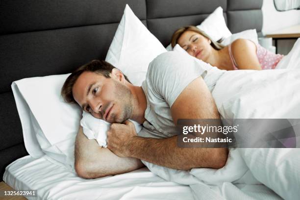 man in bed can not sleep because his wife is snoring - man sleeping on bed stock pictures, royalty-free photos & images