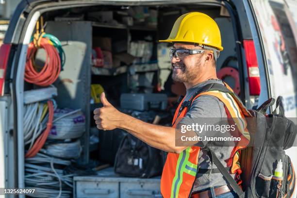 smiling hispanic construction worker wearing a work helmet looking away with his thumbs up - bestelwagen stockfoto's en -beelden