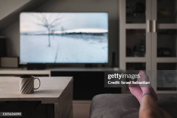 unrecognizable young caucasian girl, lying on her couch watching tv in her living room. - legs on the table foto e immagini stock