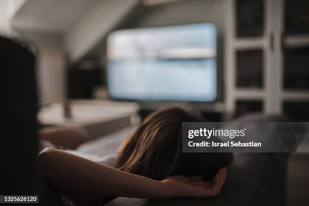 view from behind of an unrecognizable young caucasian woman lying on the couch enjoying her favorite program. - watching tv from behind stockfoto's en -beelden
