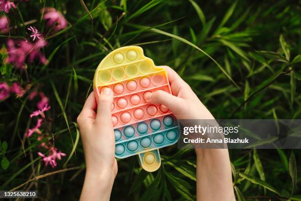 new trendy pop it fidget toy in hand for children and people with stress. rainbow pop it bubble sensory toy for kids, summer shape of ice cream. - fidget spinner stock pictures, royalty-free photos & images