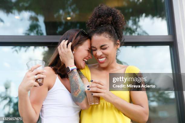 two millennial women, one caucasian with shoulder length hair and the other mixed race with curly hair, laugh while they hug each other outdoor near a building, wearing casual summer clothing. - mid length hair stock pictures, royalty-free photos & images