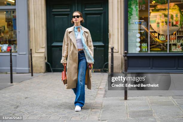 Sean Levyy wears a white ribbed crop-top / t-shirt, a pale blue shirt, a pale blue scarf, a beige long coat, blue denim ripped jeans pants, a...