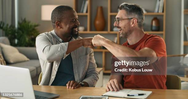 shot of two mature men giving each other a fist bump while while using a laptop at home - fist bump stock pictures, royalty-free photos & images