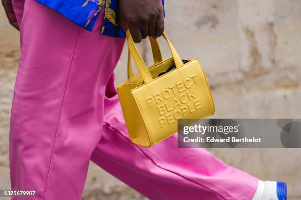 Guest wears a green blue with multicolored print pattern shirt, fuchsia pink leather pants, a yellow shiny leather hand bag with an embossed slogan...