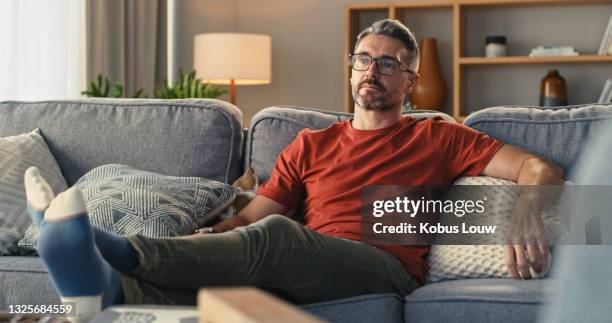 shot of a mature man relaxing on the sofa at home - man middelbare leeftijd woonkamer stockfoto's en -beelden