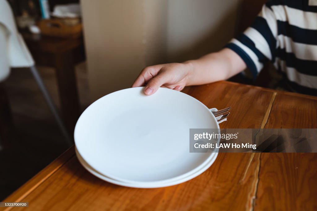 An Asian woman is distributing empty plates on a wooden table
