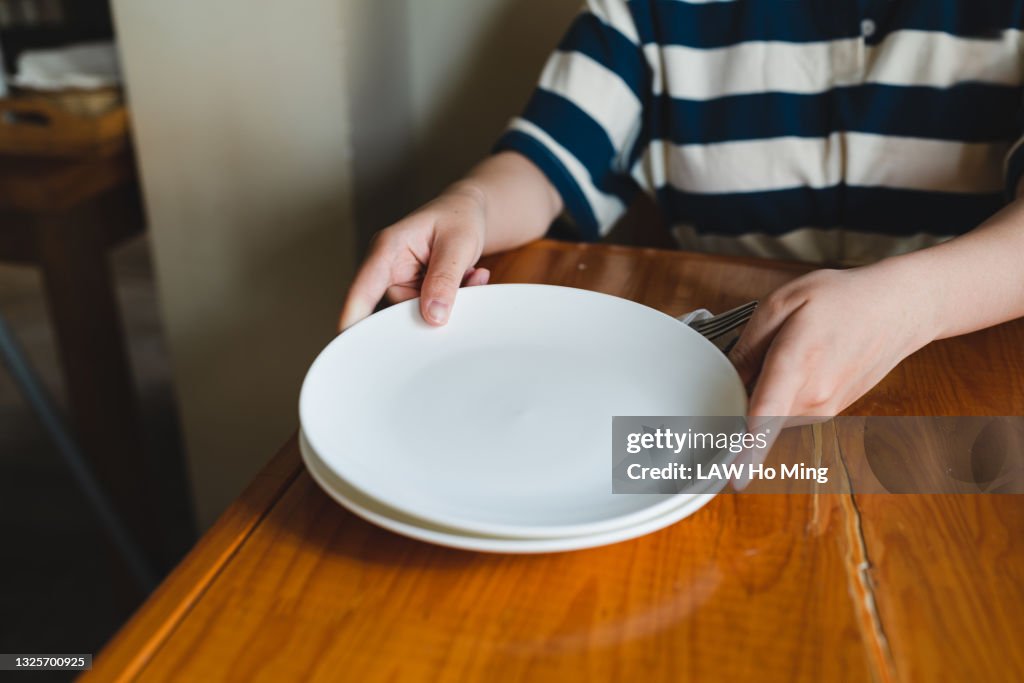 An Asian woman is distributing empty plates on a wooden table