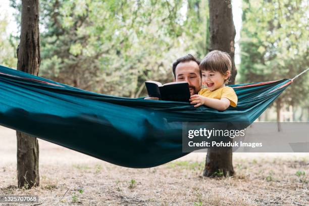 father and his son reading a book in a hammock - hammock reading stock pictures, royalty-free photos & images