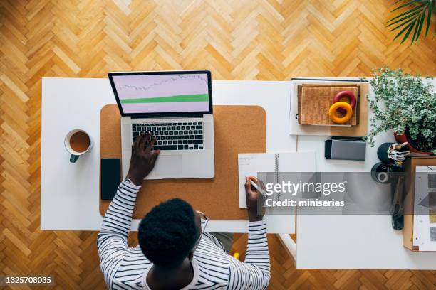 arbeit frim home: junger afroamerikaner mit laptop und notizen - adapting stock-fotos und bilder