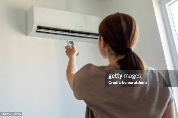 frau schaltet klimaanlage mit fernbedienung ein - hand isoliert stock-fotos und bilder