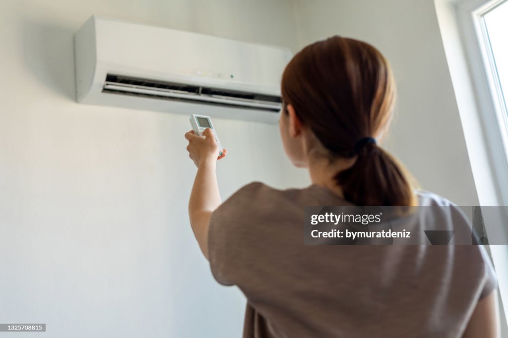 Woman turning on air conditioner with remote