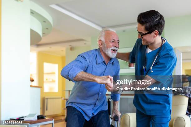 healthcare worker is in home visit to an older man with physical disabilities and assisting him to get up. - nursing assistant stock pictures, royalty-free photos & images