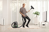 Guy in leather pants playing and dancing with a vacuum cleaner on a carpet
