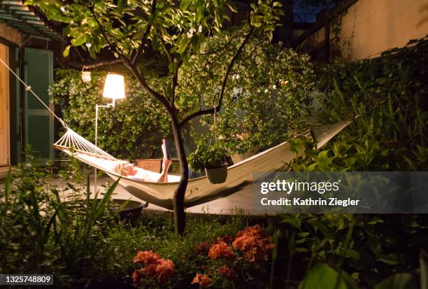 woman relaxing in hammock in back yard at night, reading a book - ruhe alltag stock-fotos und bilder