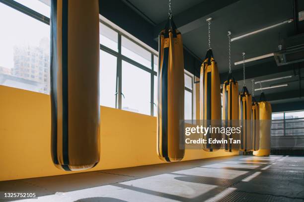 club de la salud del gimnasio con una fila de saco de arena amarillo del bolso que perfora al lado del tiempo del día de la ventana - kick boxing fotografías e imágenes de stock