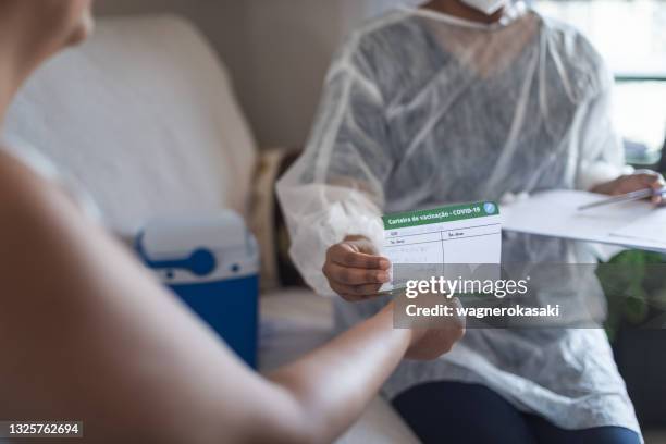 vaccination at home. female nurse giving the vaccination record card ("carteira de vacinação", written in portuguese) to patient - vacinação stock pictures, royalty-free photos & images